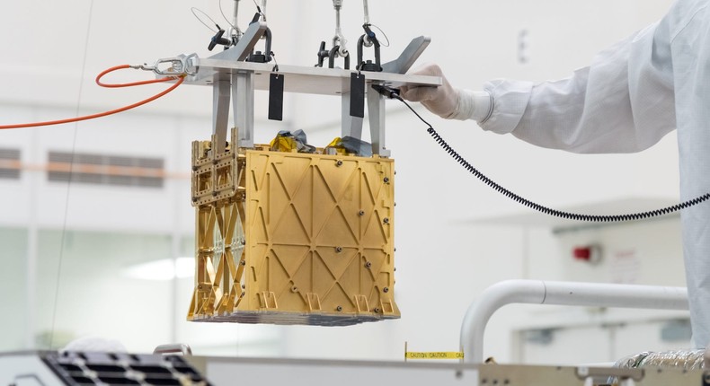 Technicians in the cleanroom at NASA's Jet Propulsion Laboratory lowering the MOXIE instrument into the belly of the Perseverance rover.
