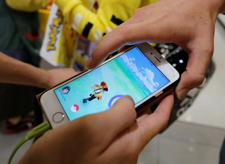 Men play the augmented reality mobile game "Pokemon Go" by Nintendo on a mobile phone in Tokyo