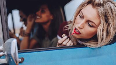 Ładna kobieta ze szminką przegląda się w samochodowym lusterku