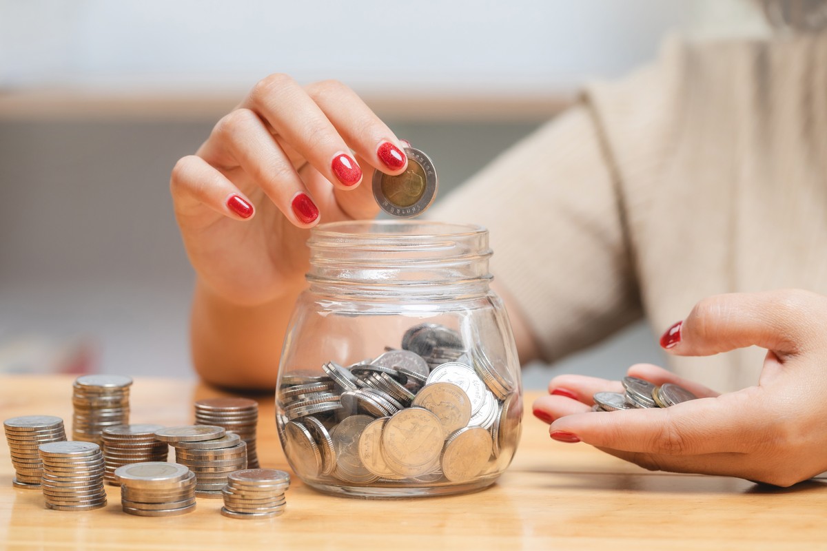 Kobieta ręcznie wkłada monety do szklanej butelki dla oszczędności pieniędzy, bogactwa i koncepcji finansowej, inwestycji.