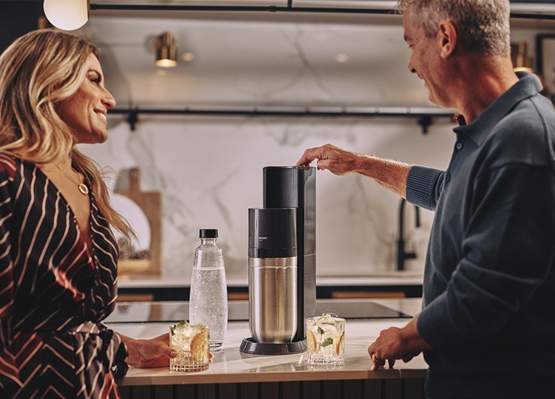 Kobieta i mężczyzna stojący przy saturatorze SodaStream Duo w kuchni - zdjęcie