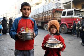 Children carry cooked meals provided by the UN through a partner NGO at al-Mashatiyeh neighborhood o