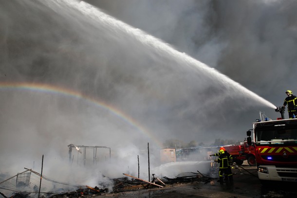 A rainbow is seen as firmen work to extinguish burning makeshift shelters in the Jungle on the thi