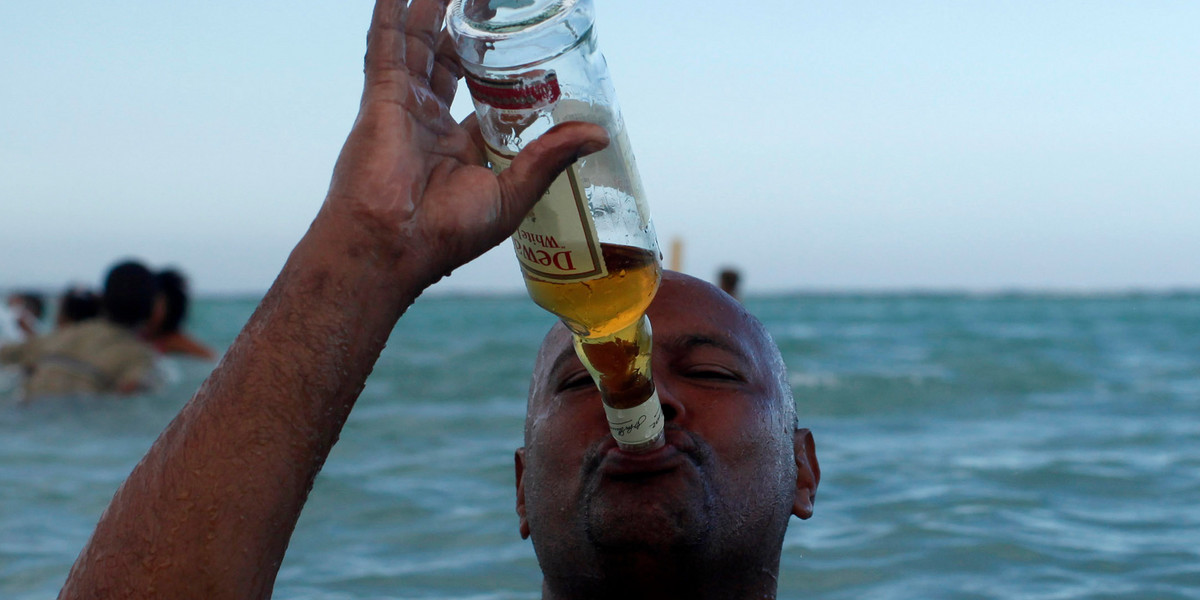Resident drinks whiskey from the bottle while in the sea at a beach in Boca Chica