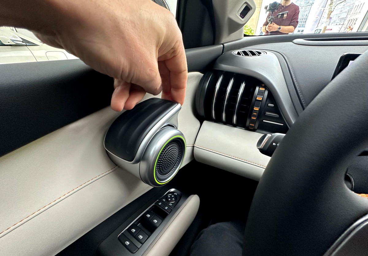 Zbliżenie na unikalny detal wnętrza chińskiego SUV-a BYD ATTO 3 EVO: klamka wewnętrzna drzwi zintegrowana z głośnikiem. Widoczna jest dłoń autora testu, która demonstruje sposób otwierania drzwi. Rozwiązanie łączy funkcjonalność z nowoczesnym designem