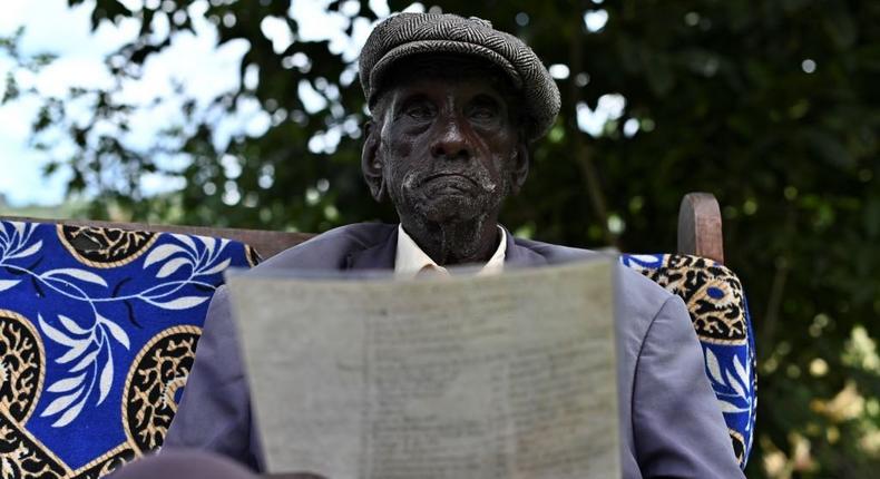 Kibore Cheruiyot Ngasura, 95, sits in his compound with an old picture, bearing names of his clansmen whom he was forcefully evicted with from their lands, at his farm in Tugunon village, Kipkelion in Kenya's Kericho highlands, Kericho county, on October 8, 2019. - (Photo by TONY KARUMBA/AFP via Getty Images)