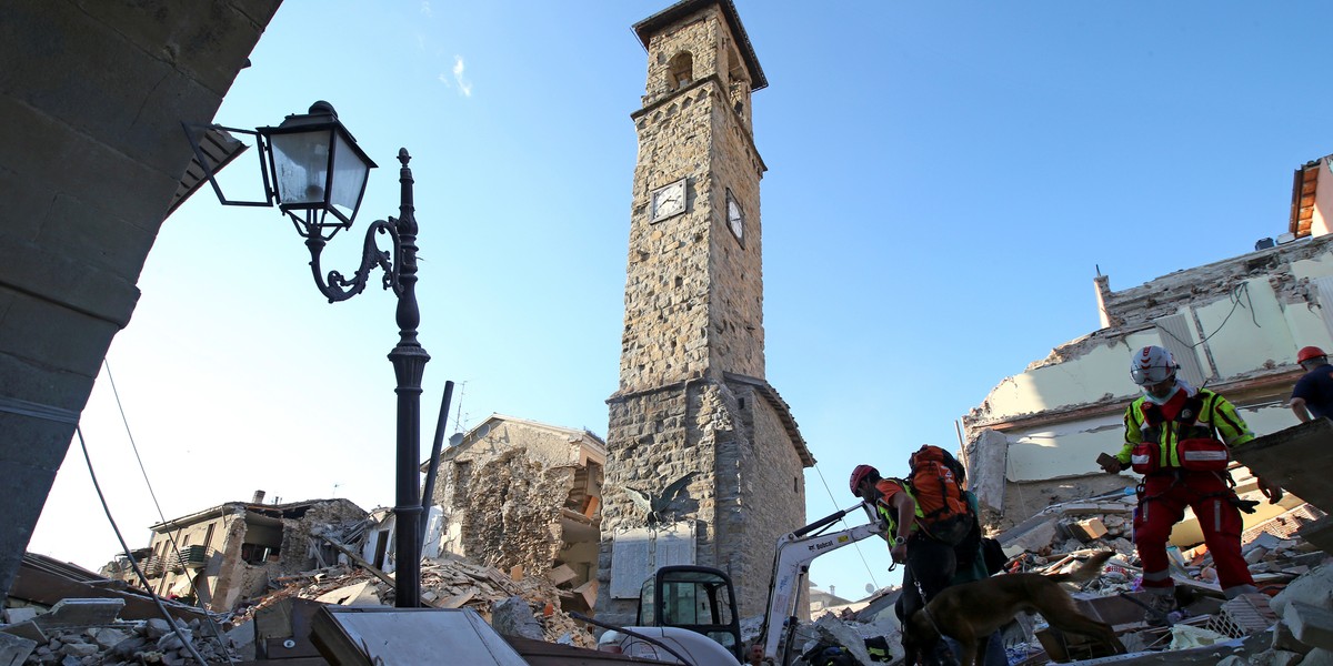 Rescuers walk past the tower with the clock showing the time of the earthquake on August 24.