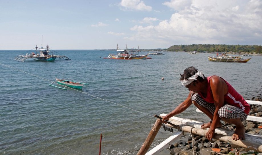 A fisherman repairs his boat overlooking fishing boats that fish in the disputed Scarborough Shoal in the South China Sea, at Masinloc, Zambales, in the Philippines.