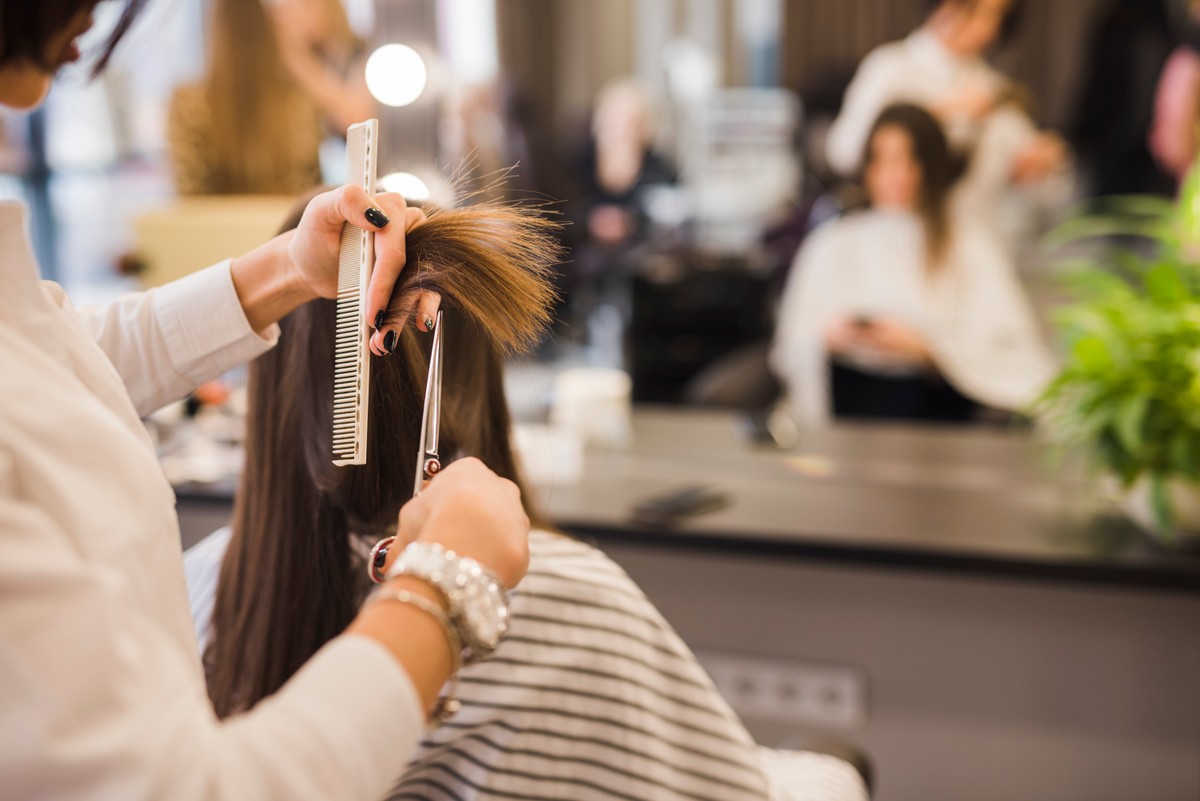 Fryzjer wykonujący usługę strzyżenia włosów w salonie fryzjerskim, klientka siedzi przed lustrem. Świadczenie usług na działalności nierejestrowanej może wiązać się z obowiązkiem zgłoszenia tego do ZUS.