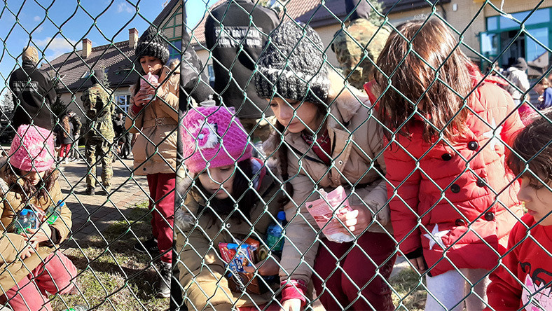 Dzieci migrantów odbierają produkty pod siatką ogrodzenia. 