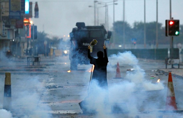 A female protester holding a photo of Shi'ite scholar Isa Qassim as she confronts riot police armour