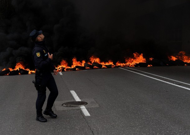 A member of riot police walks in front of a flaming barricade during a May Day rally in Gijon