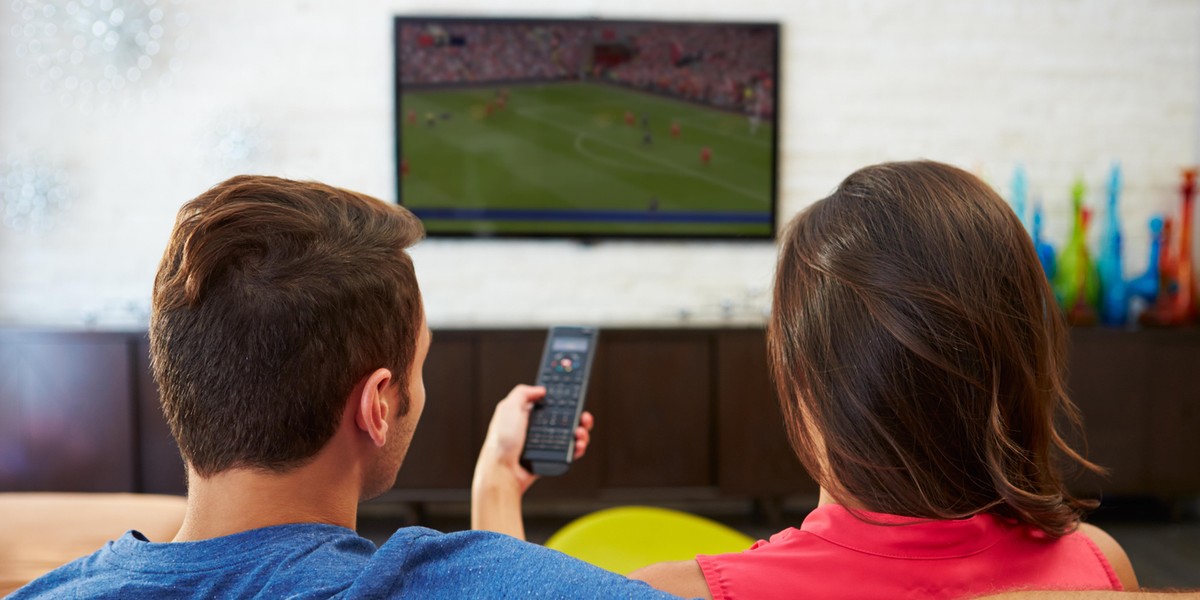 Rear View Of Couple Sitting On Sofa Watching TV Together