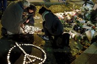 People kneel as they light candles to pay tribute to victims near the site of the attack at the Bata