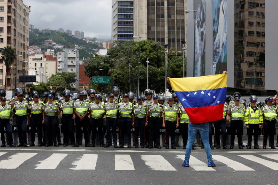 An opposition supporter stands with the Venezuelan flag in front of police during a rally to demand a referendum to remove President Nicolas Maduro in Caracas, July 27, 2016.