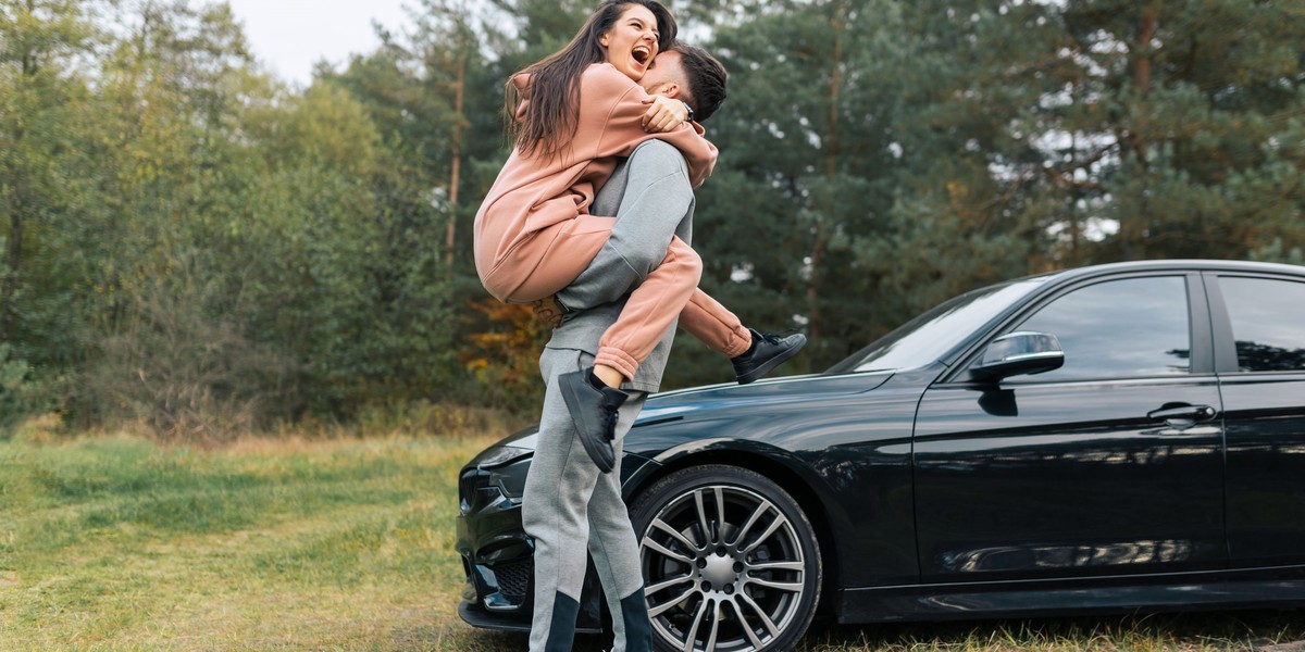 Beautiful young couple in tracksuits near their car. Happiness girl in the arms of her boyfriend