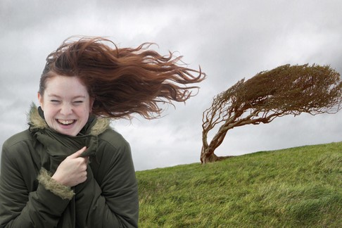 Young woman standing on windswept hill, smiling, eyes closed