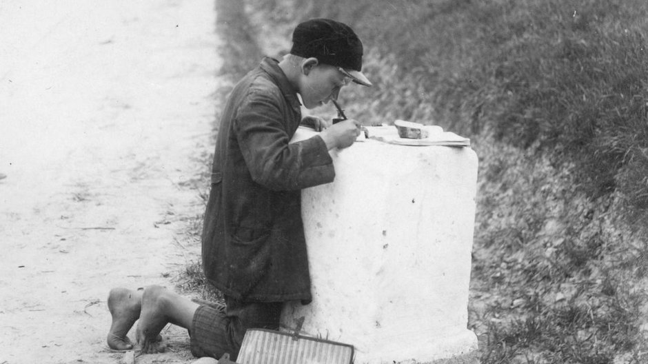 Uczeń podczas odrabiana lekcji przy kamieniu kilometrowym Zdjęcie z początku lat 30. XX wieku.