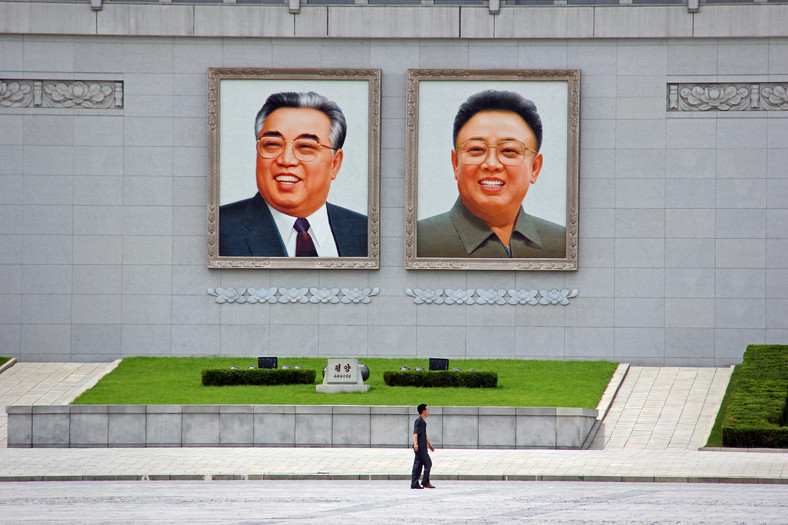 Samotny przechodzień obok wielkich portretów Kim Ir Sena i Kim Dzong Ila w Pjongjangu