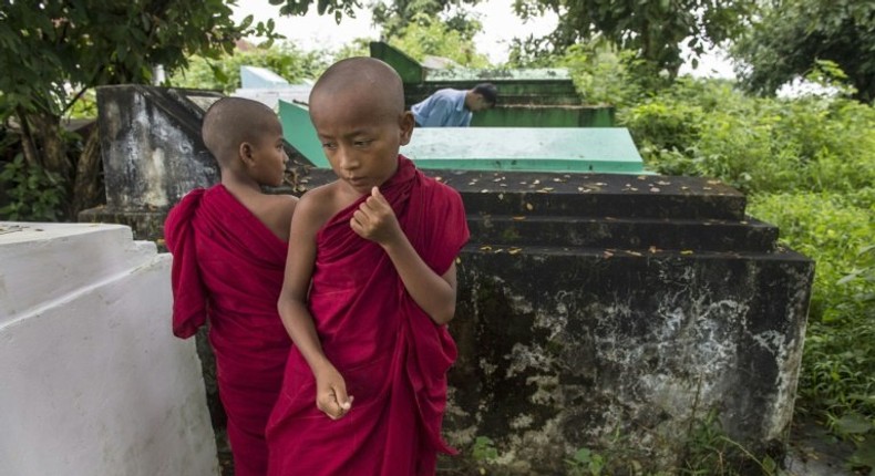 Cemetery personnel bury the body of a three-year-old child, one of three victims of an exorcism ritual in Twante, south of Yangon on October 22, 2016, as young novice monks looks on