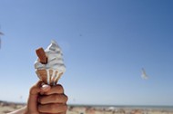 Man holding ice cream on beach, close-up of hand