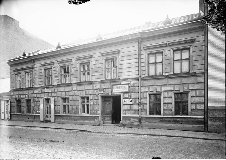 Kamienica nr 26 na Ulicy Krupniczej w Krakowie. Fragment ulicy. Dom, w którym urodził się Stanisław Wyspiański. Widoczne szyldy pracowni stolarskiej Teodora Janika, akuszerki - J. Przybyłowej, szefca - Franciszka Zawady, malarza - Stanisława Karasia, mleczarni - Z. Mazgajewskiej oraz sklepu wiejskiego