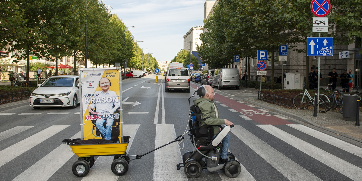 Łukasz Krasoń ciągnie po Warszawie swój baner wózkiem elektrycznym. Po co idzie do polityki?