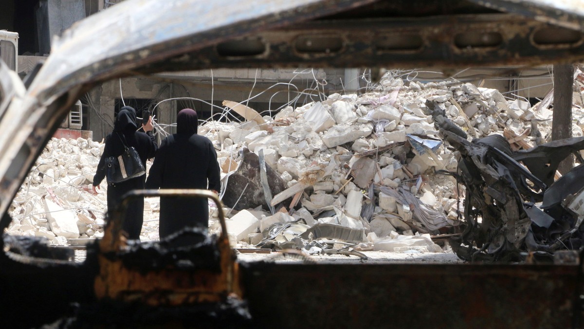 Women walk past damage near al-Quds hospital after it was hit by airstrikes, in a rebel-held area of Syria's Aleppo