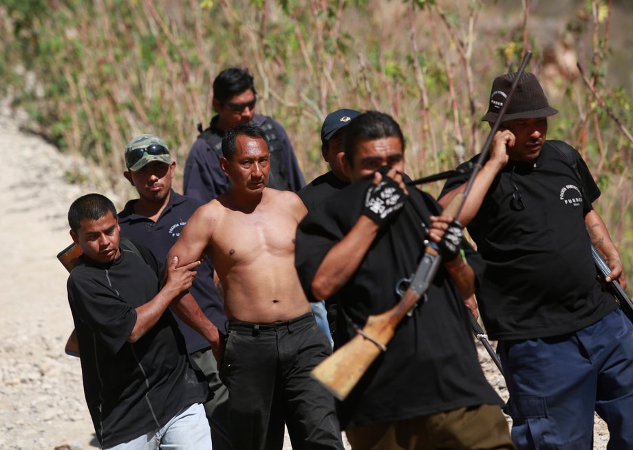 Members of the Community Police of the FUSDEG (United Front for the Security and Development of the State of Guerrero) walk with a man they captured after a shootout against a group that villagers suspect are members of a local gang, at a hill in the village of Petaquillas, on the outskirts of Chilpancingo, Guerrero, February 1, 2015.