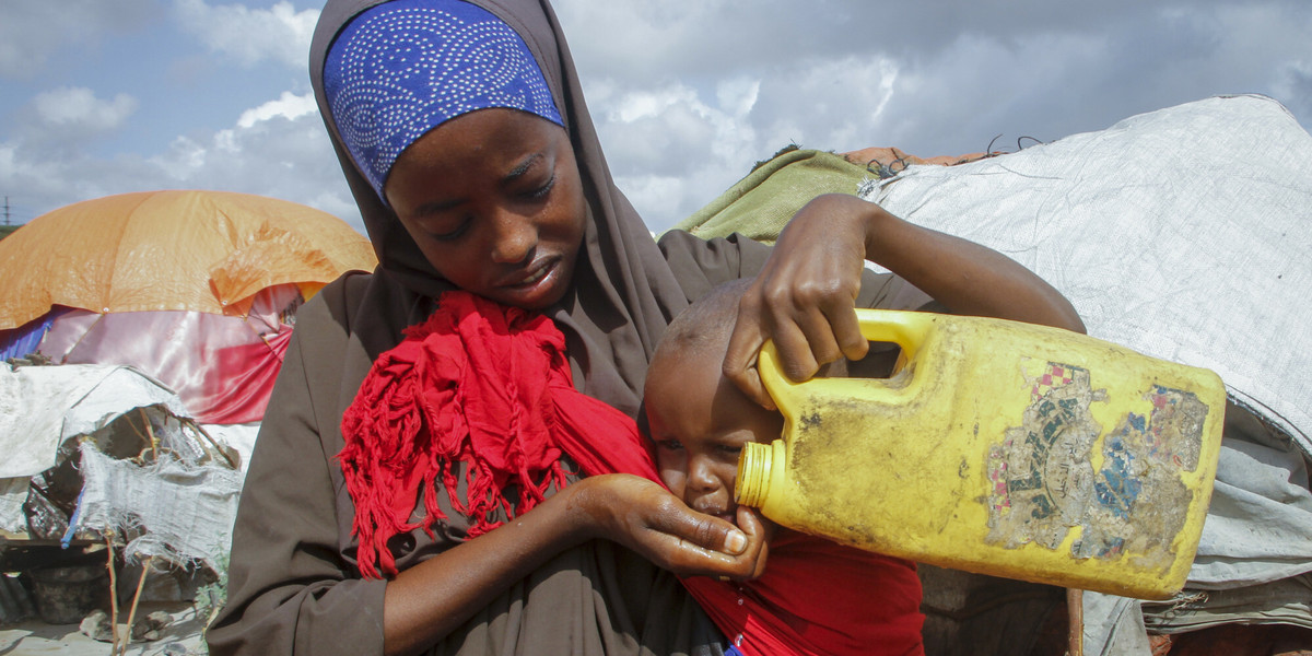 Somalijska kobieta, która uciekła z obszarów dotkniętych suszą, podaje wodę swojemu dziecku. Zdjęcie zrobione w obozie dla wysiedleńców na obrzeżach Mogadiszu w Somalii w sobotę, 4 czerwca 2022 r.