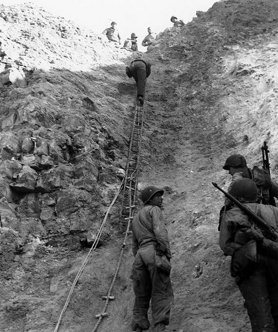Amerykańscy Rangersi z mozołem wspinają się na Pointe du Hoc. Przyczółek udało się ostatecznie zdobyć (6 czerwca 1944, domena publiczna).