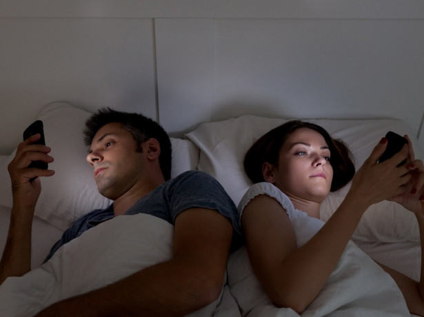 Kobieta i mężczyzna w łóżku trzymają smartfony