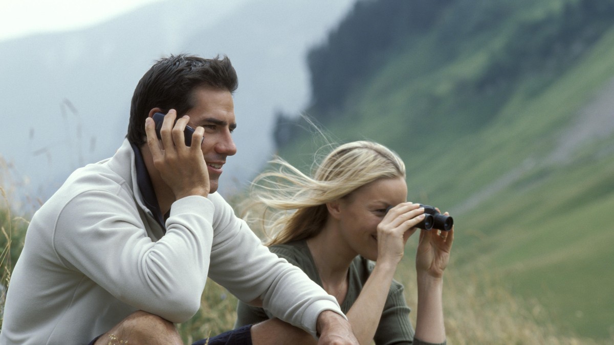 Man with cell phone and woman with binoculars