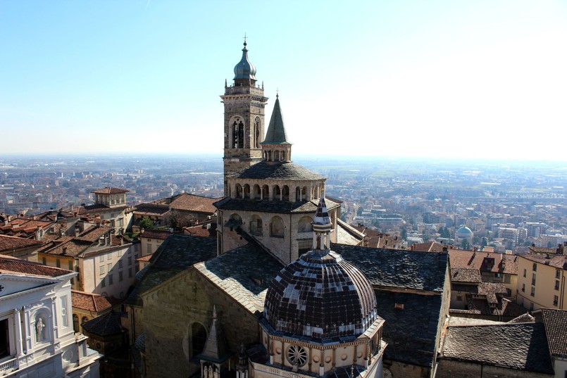 W Bergamo można wyróżnić dwa najważniejsze miejsca, a jednym z nich jest Piazza del Duomo. To tu znajduje się sławna katedra, będąca niekwestionowanym symbolem miasta. Santa Maria Maggiore to niesamowity kościół, którego budowa rozpoczęła się w XIII wieku. Zwiedzenie go dla tego, kto odwiedza Bergamo po raz pierwszy, może być sporym zaskoczeniem. Świątynia bowiem od zewnątrz jest typowym przykładem architektury romańskiej - bardzo monumentalnej, ale surowej, wewnątrz natomiast dominuje styl barokowy. W porównaniu ze skromną fasadą, niesamowicie zdobione sufity, bogate kaplice i ołtarze robią ogromne wrażenie. Warto przyjrzeć się także dwóm lwom, które znajdują się przed wejściem do kościoła. Stanowią one symbole miasta. Sama katedra została wybudowana w podziękowaniu za zażegnanie epidemii dżumy, ma więc dla mieszkańców szczególne znaczenie. Co ciekawe, katedra w Bergamo była przez długi czas najbardziej rozpoznawalnym na świecie miejscem w miasteczku. Swoją popularność zawdzięczała temu, jaką rolę odegrała w rozwoju muzyki. Od średniowiecza mieściła się tu jedna z najważniejszych szkół muzycznych w Europie, do której zjeżdżano z całego kontynentu. Wszystko to dlatego, że Santa Maria Maggiore może poszczycić się bardzo dobrą akustyką.