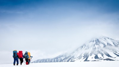 Group with gear and backpacks crossing icy field to mountain