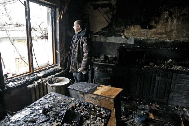 Local resident looks out of window at his house damaged by shelling, in Donetsk