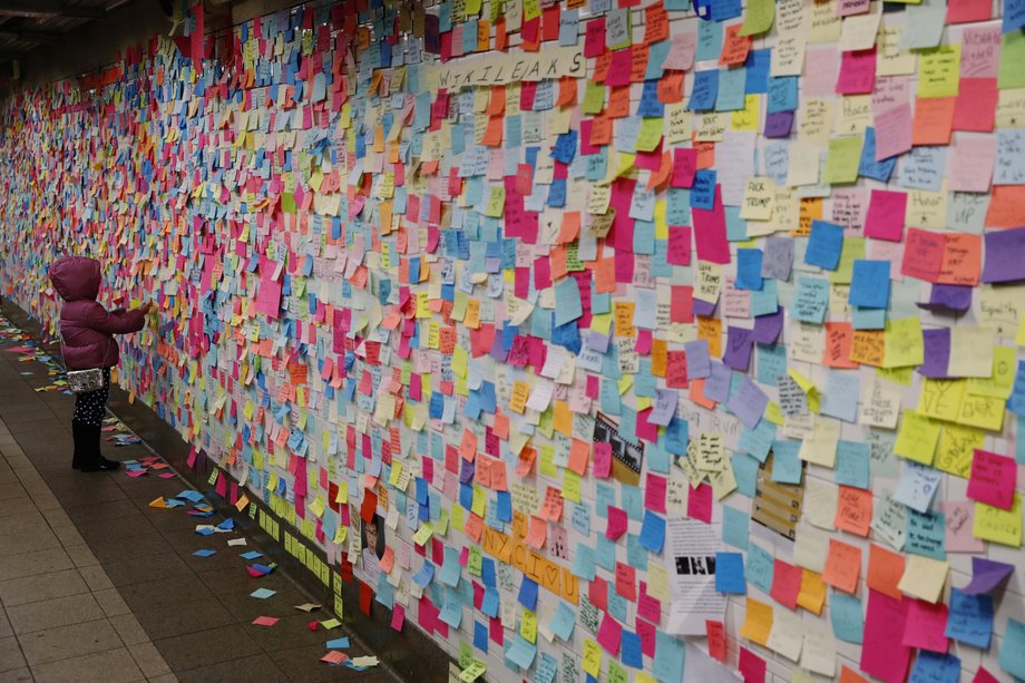 A young girl adds a message written on a post-it note to a display that was started in reaction to the election of President-elect Donald Trump in New York, U.S., November 15, 2016.