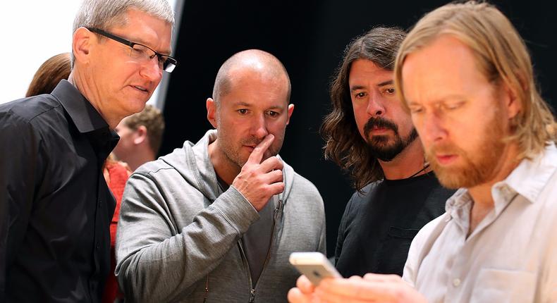 Apple CEO Tim Cook, head designer Jony Ive, and Foo Fighters frontman Dave Grohl look at an iPhone.