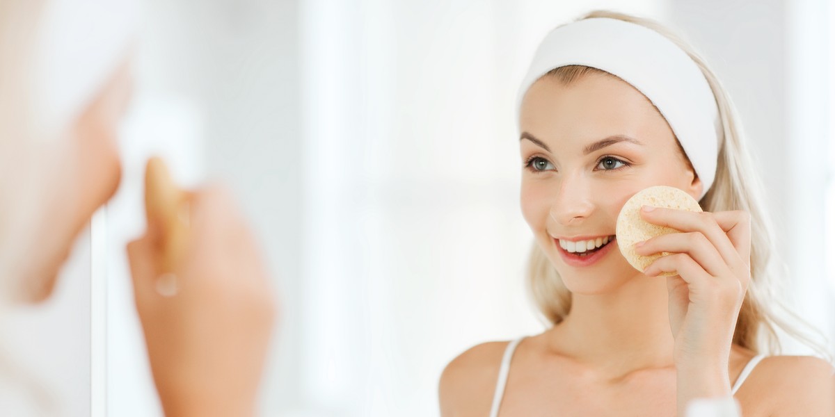 young woman washing face with sponge at bathroom