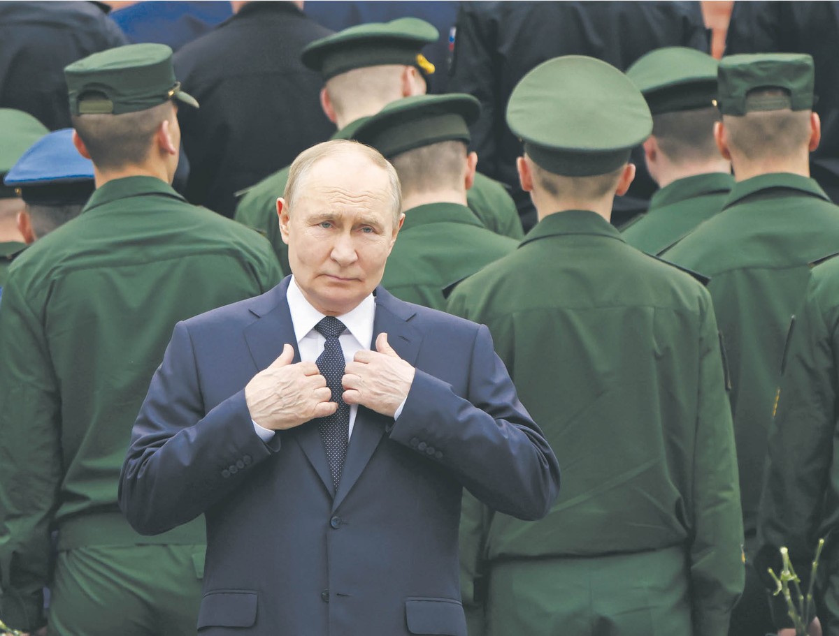 Putin w garniturze trzyma się za klapy marynarki. Za nim widać stojących rosyjskich żołnierzy