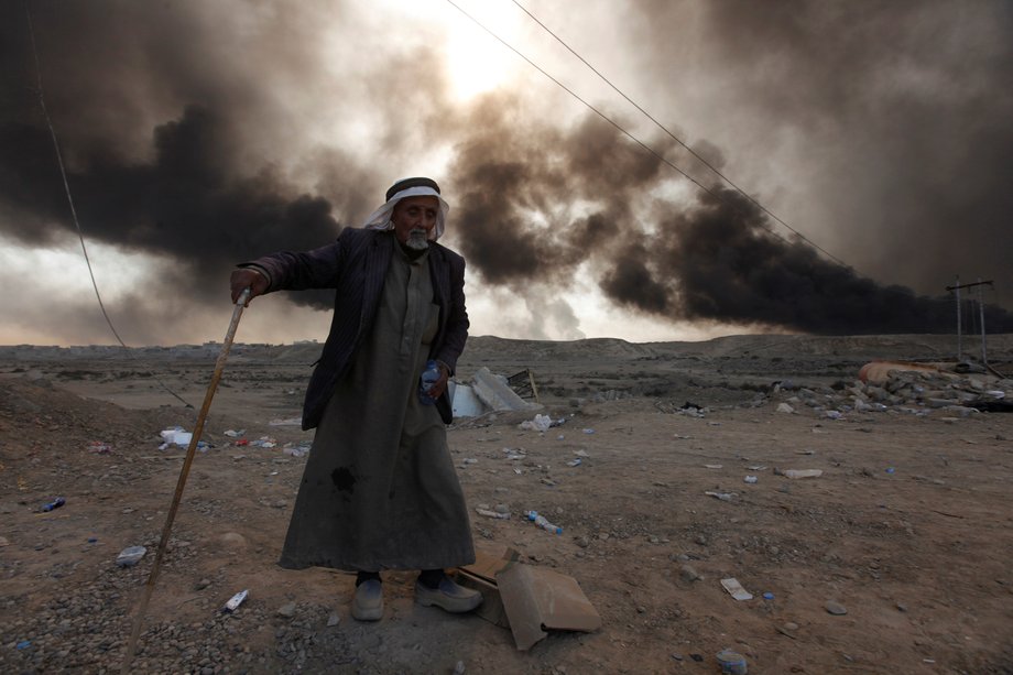 A man returns to his village after it was liberated from ISIS, south of Mosul in Qayyarah, Iraq, October 22, 2016. The fumes in the background are from oil wells that were set ablaze by ISIS militants.