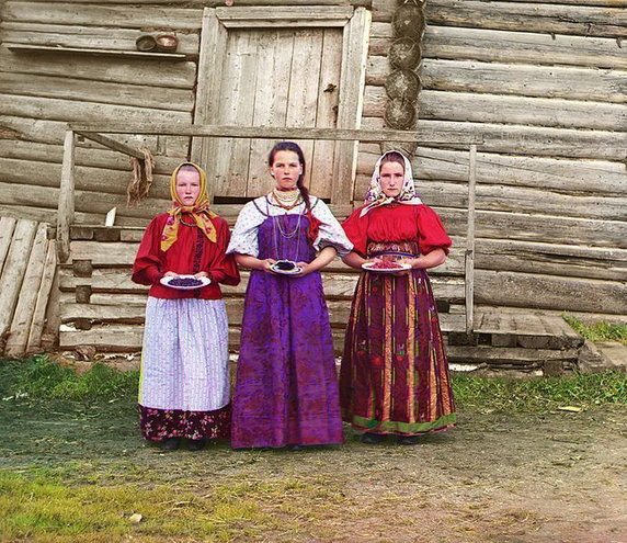 Młode rosyjskie chłopki przed tradycyjnym drewnianym domkiem, wieś nad rzeką Szeksną niedaleko miasteczka Kiriłłow (1909, domena publiczna).