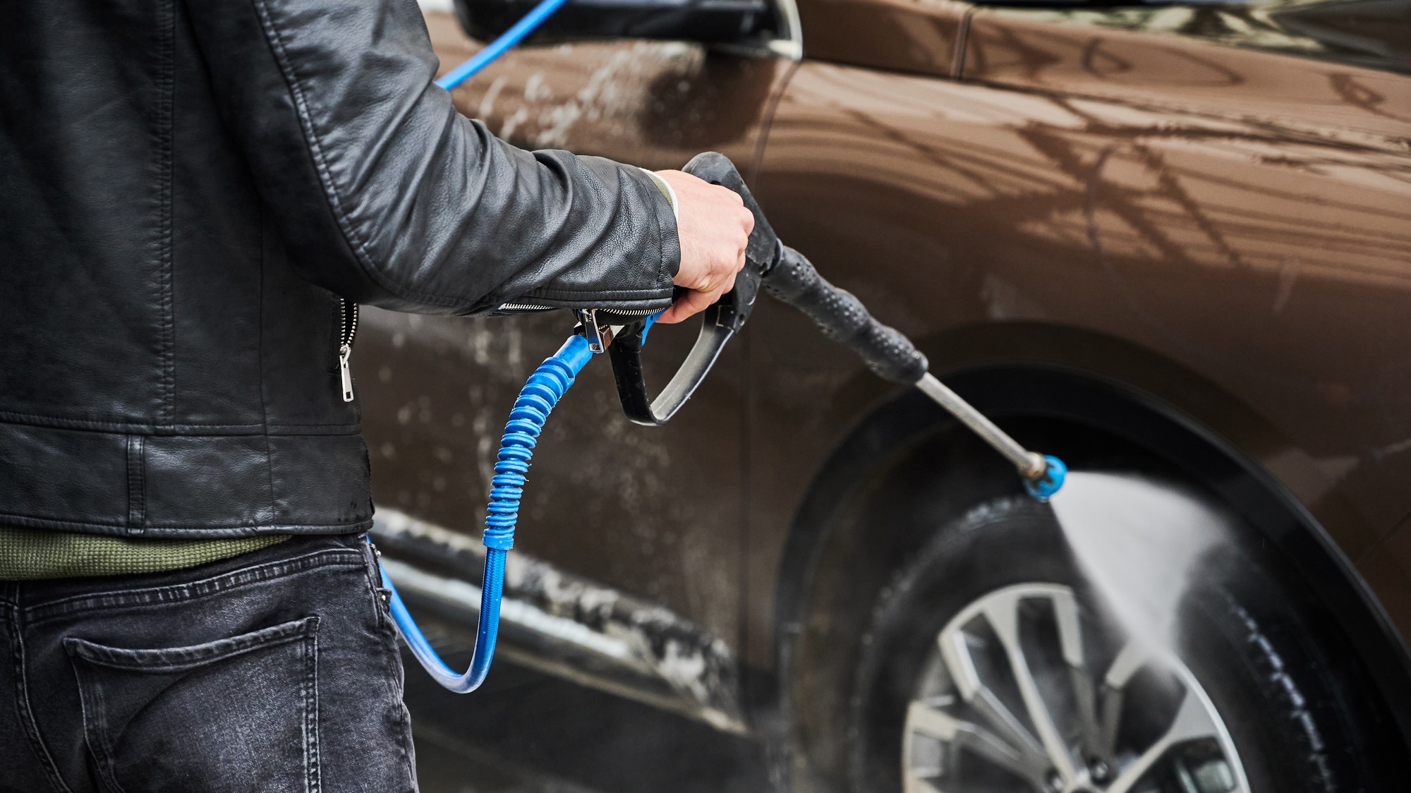 Vodič umýva auto na ručnej autoumyvárke pomocou vysokotlakovej pištole. 