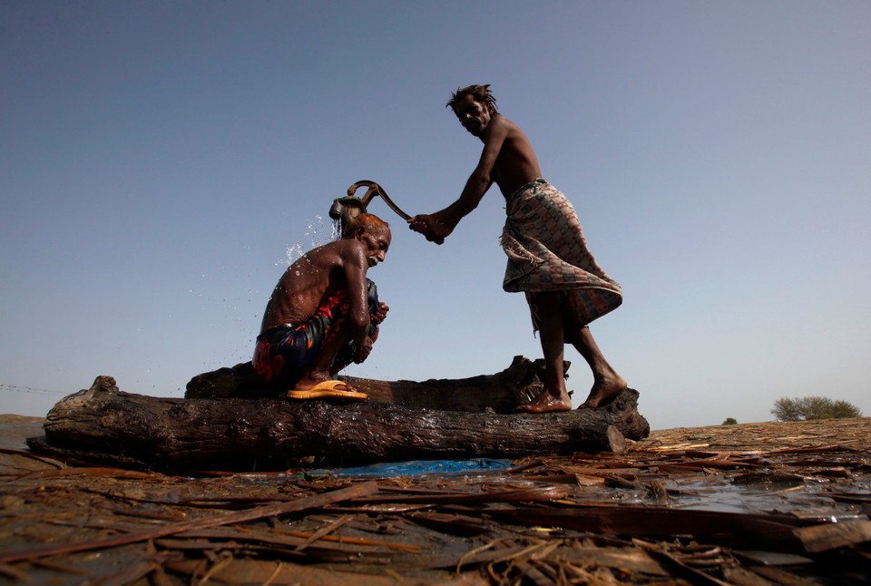 Villagers, displaced by flooding, take a bath at a hand pump while taking refuge on an embankment near the flooded village of Bello Patan