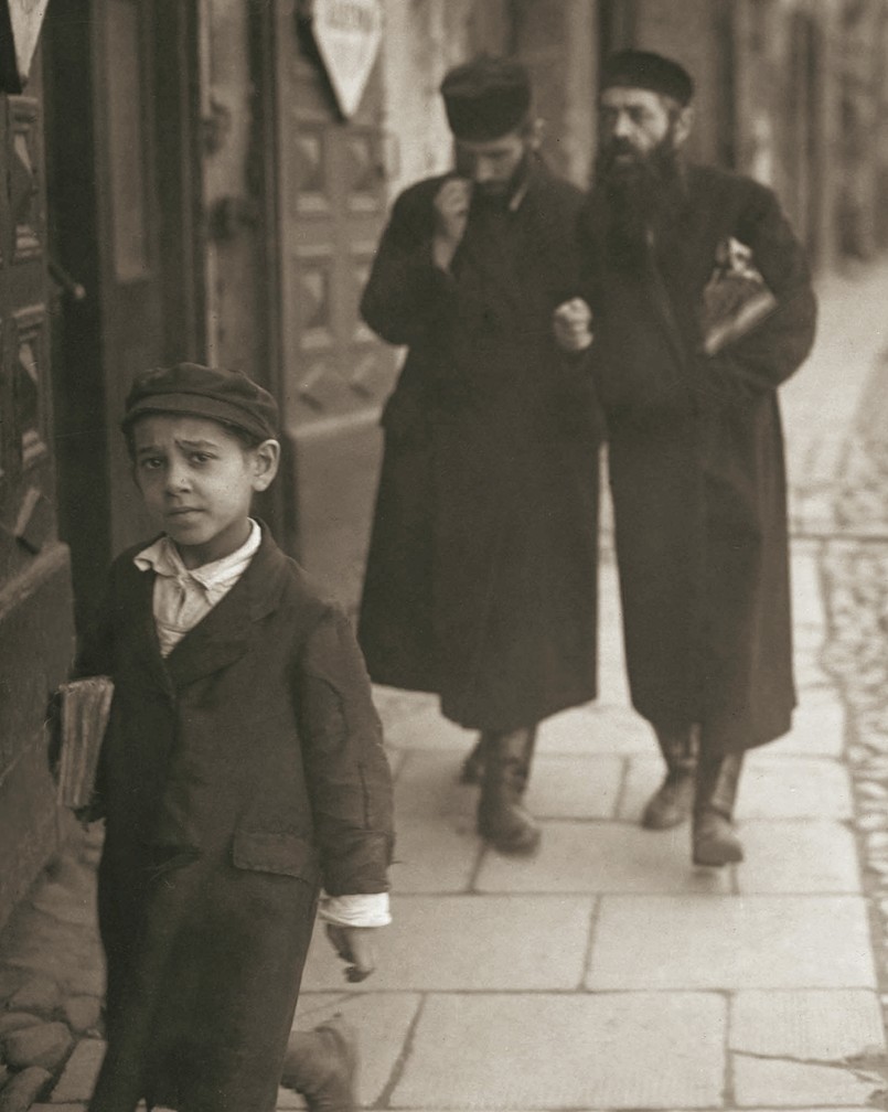 Mały chłopiec wchodzący do bramy domu przy ul. Świętojerskiej 5 wraca z zajęć w chederze, trzymając pod pachą książkę. Za jego plecami przechadza się para studentów jesziwy, z powagą dyskutujących na tematy talmudyczne. Radosny, wolny od nauki w szkołach religijnych 33 dzień omeru, czyli siedmiotygodniowego okresu liczonego pomiędzy świętami Pesach i Szawuot, wypadał w pierwszych dniach maja i zwał się lag ba-omer, z czego wzięła się znana ze współczesnej gwary uczniowskiej „laba”. Fotografia z września 1926 r. Wydawnictwo RM