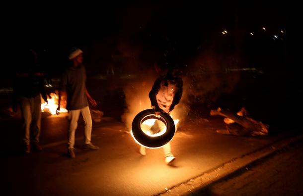 A man blocks a road with a burning tyre while protesting against electricity cuts in Klipspruit Sowe