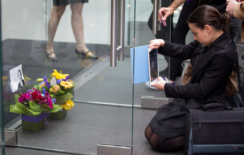 Kobieta robiąca iPadem zdjęcie kwiatom upamiętniającym śmierć Steve'a Jobsa przed sklepem Apple'a w Sydney, fot. Ian Waldie/Bloomberg