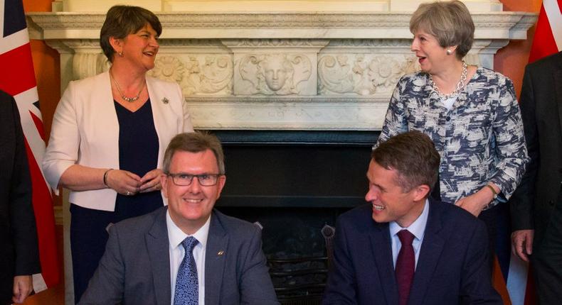 Britain's Conservative party leader and Prime Minister Theresa May (R) stands next to Democratic Unionist Party (DUP) leader Arlene Foster (L), as DUP MP Jeffrey Donaldson (2L) sits and signs paperwork with Britain's Parliamentary Secretary to the Treasury, and Chief Whip, Gavin Williamson, whilst posing for a photograph inside 10 Downing Street in central London on June 26, 2017.