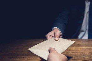 A man giving bribe money in a brown envelope to another businessman in the dark