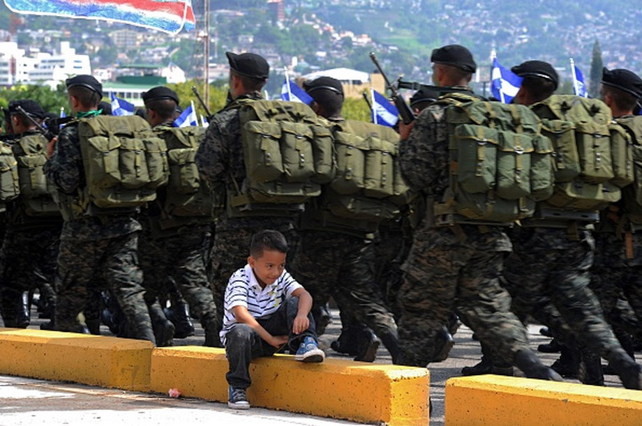 A child sits next to Honduran soldiers as they take part in a military parade during the commemoration of the Soldier Day in Tegucigalpa, on October 3, 2015.